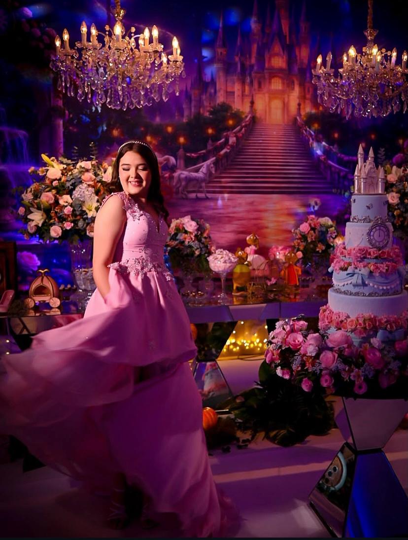 Debutante de vestido rosa girando diante de cenário de castelo com bolo temático
