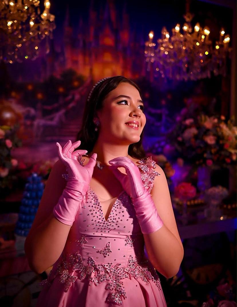 Debutante de vestido rosa e luvas sorrindo diante de cenário de castelo
