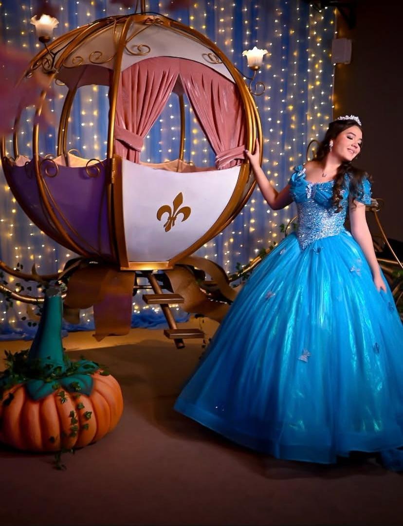 Debutante de vestido azul ao lado de carruagem dourada de Cinderela
