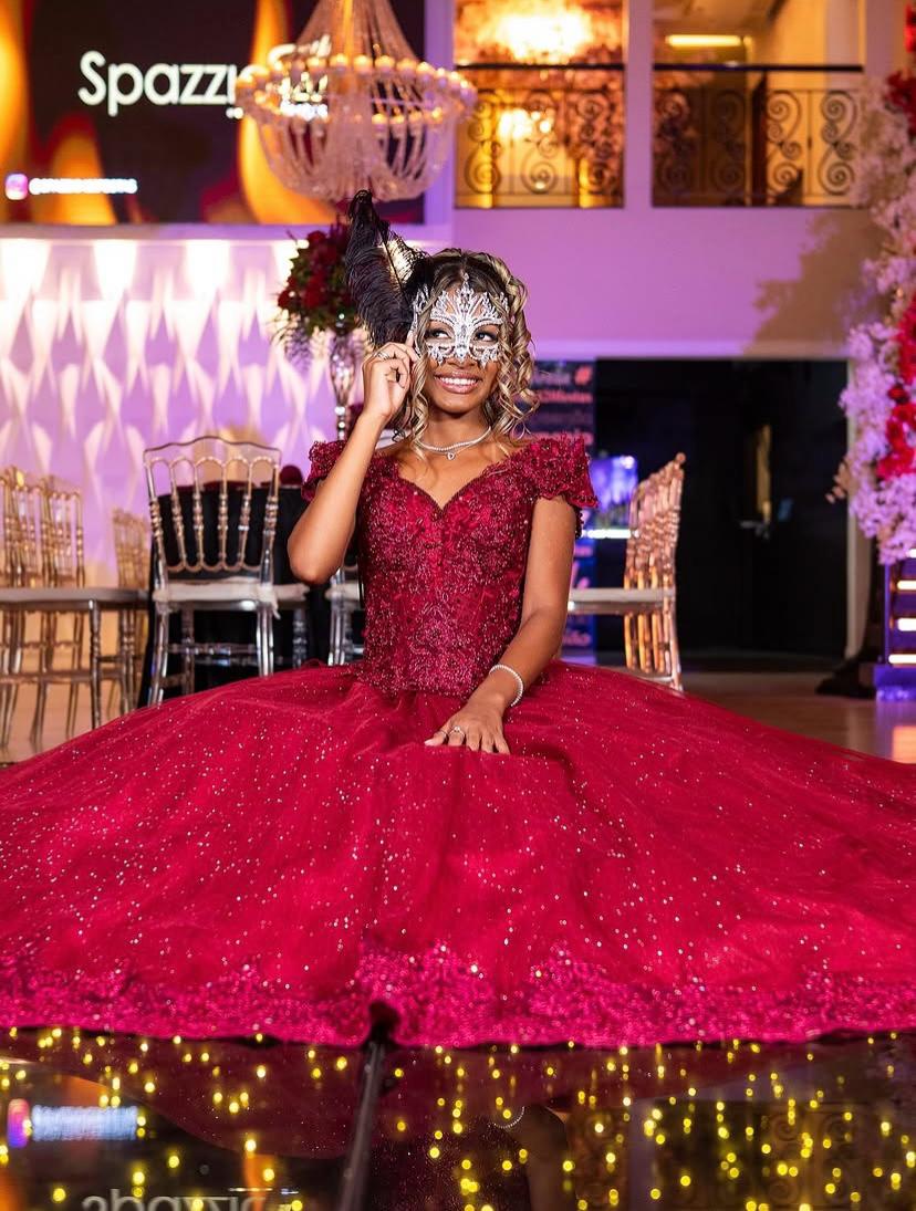 Debutante de vestido vermelho com máscara prateada sentada na pista iluminada